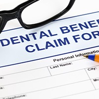 Blue top of dental insurance claim form with black framed glasses and pen