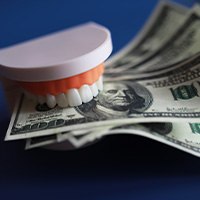 Artificial teeth holding several $100 bills with dark blue background