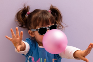 Little girl rocking a pair of shades and blowing a fantastic bubblegum bubble