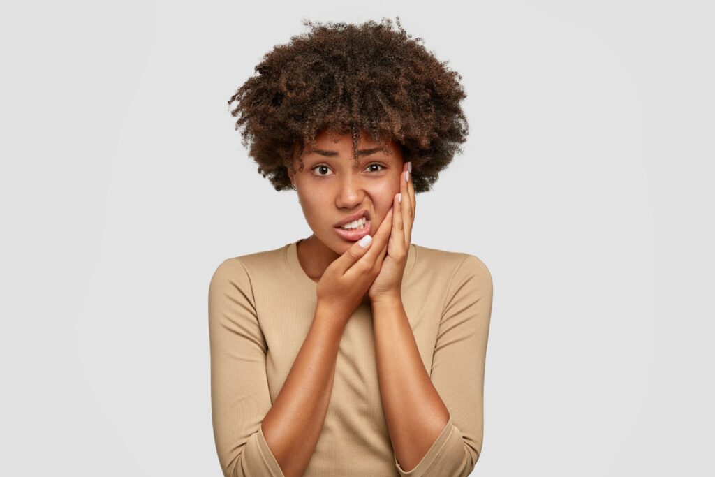 Woman in tan shirt holding side of her face in pain